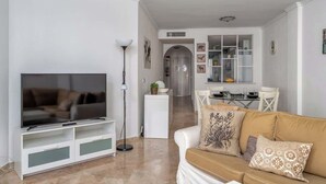 Een moderne woonkamer met een flatscreen televisie, een bank en een eethoek met een tafel en stoelen.