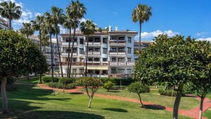 Een meerlaags hotel met balkons, omgeven door verzorgde gazons en palmbomen.