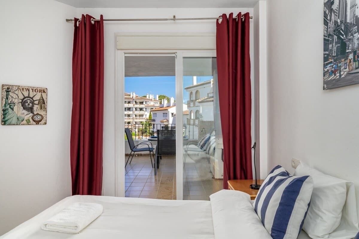 A hotel room with a bed, a view of a cityscape through a glass door, and a red curtain.