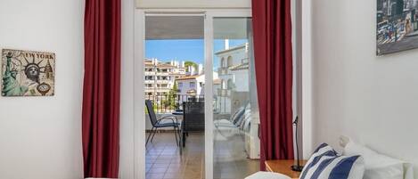 A hotel room with a bed, a view of a cityscape through a glass door, and a red curtain.