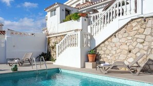 Une piscine bordée d’un mur en pierre et un bâtiment blanc doté d’un balcon.
