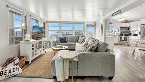 Ein modernes Wohnzimmer mit grauem Sofa, Fernseher und Meerblick.