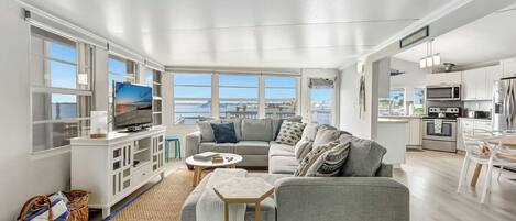 A modern living room with a grey sofa, a TV, and a view of the sea.