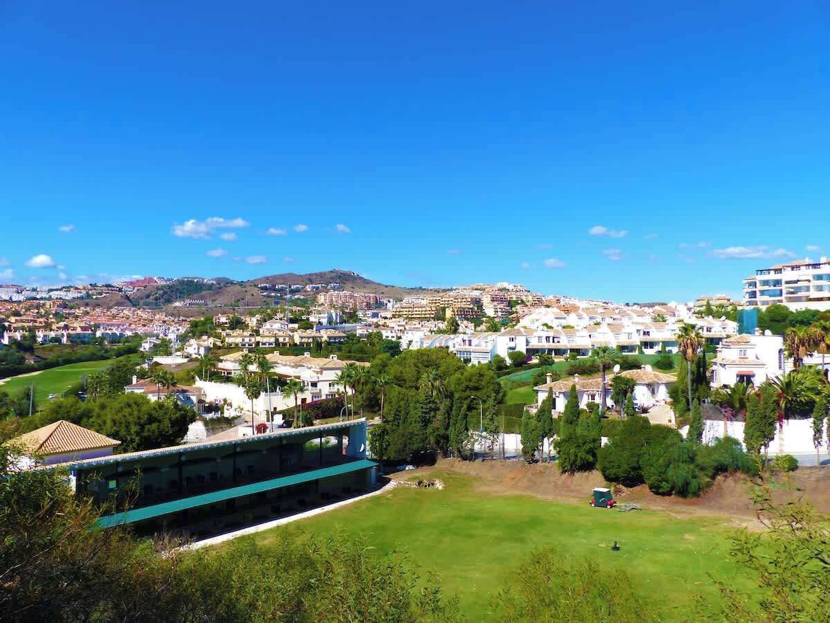Una località costiera con edifici residenziali e commerciali, un edificio blu in primo piano e un cielo azzurro limpido.