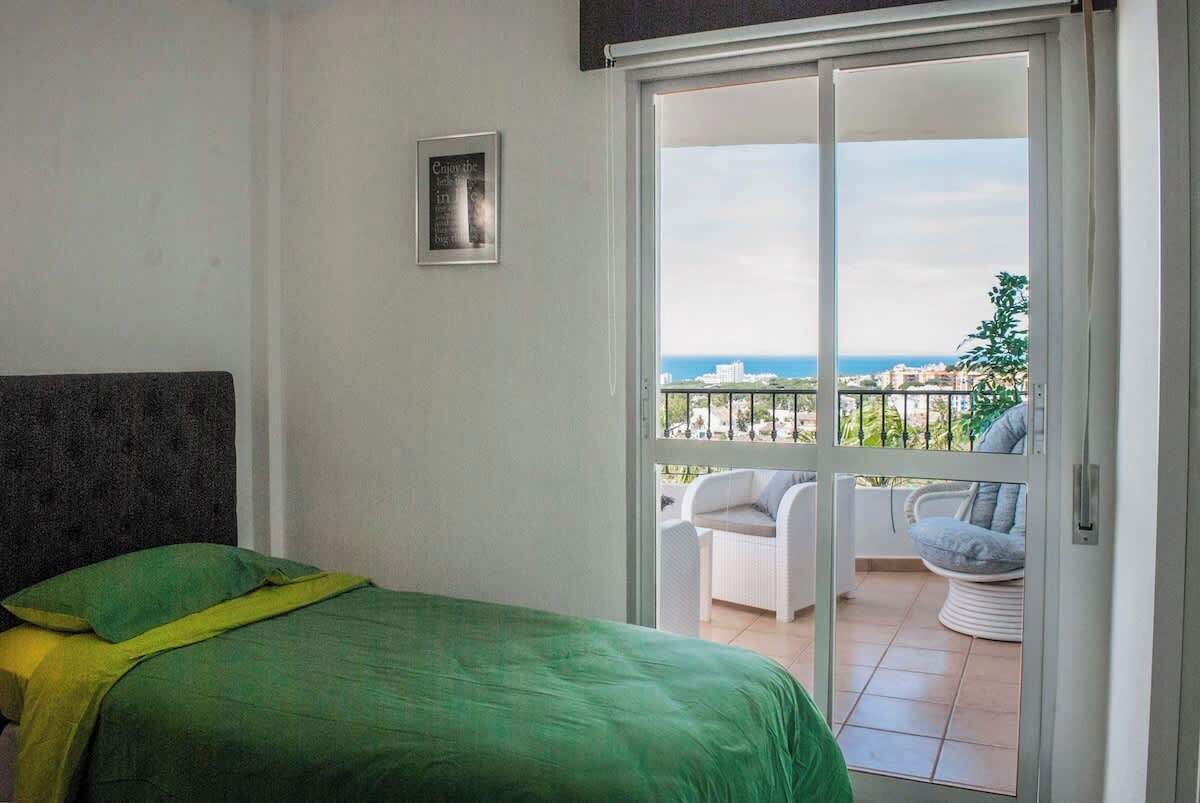 Un dormitorio con cama, puerta corrediza de vidrio que da a un balcón con mobiliario exterior.