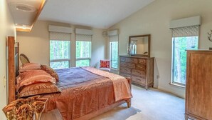 Un dormitorio con una cama grande, un aparador, un espejo y ventanas con cortinas.