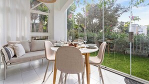 Un coin repas avec une table dressée pour quatre personnes, un canapé et une grande fenêtre donnant sur un jardin.