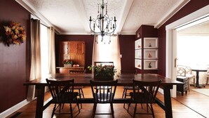 Un comedor con mesa y sillas de madera, una araña y vista a la cocina.