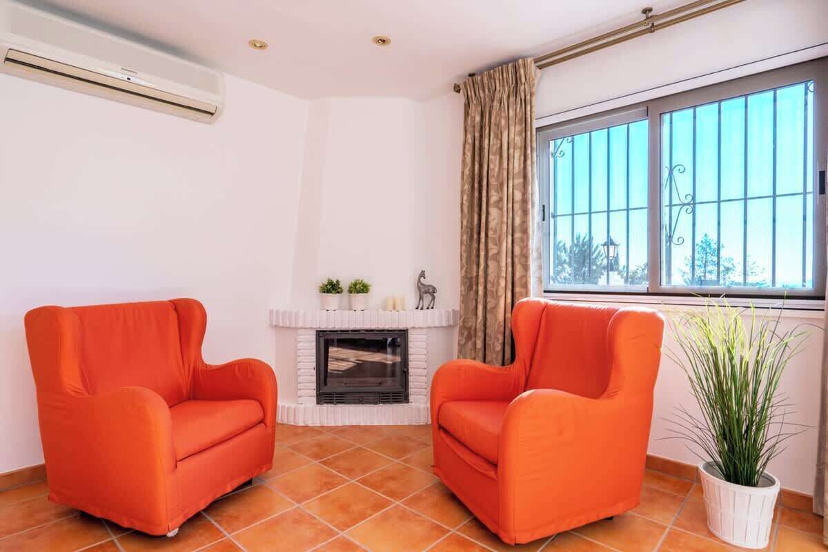 A living room with two orange armchairs, a white fireplace, a window with curtains, and a potted plant.