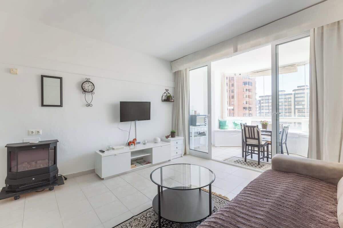 Una sala de estar moderna con un sofá, una mesa de centro de vidrio, un televisor, una chimenea y un balcón con vistas a edificios.