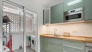 Una cocina moderna con horno integrado, un lavabo y una lavadora en la habitación contigua.