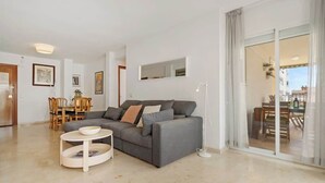 Una sala de estar moderna con un sofá gris, una mesa de centro redonda y un comedor con mobiliario de madera.