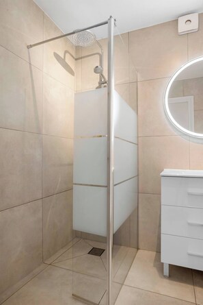 Un baño moderno con ducha envuelta en vidrio, tocador blanco y espejo redondo.