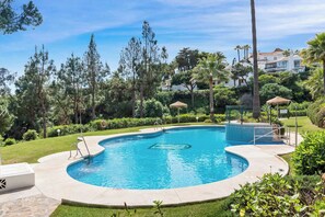 Una piscina con borde curvo, rodeada de un césped cuidado, palmeras y un edificio al fondo.