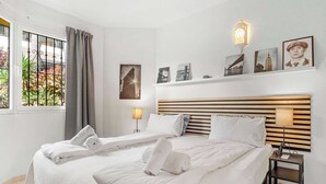 Habitación de hotel con dos camas, una ventana con cortinas, una mesita de noche con lámpara y decoración en la pared.