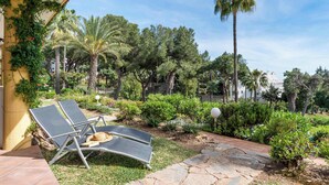 Un patio con sillones de descanso, un sendero de piedra y una variedad de follaje, incluyendo palmeras y arbustos.