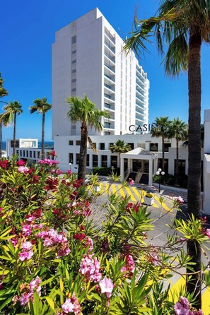 A modern hotel with a white facade, multiple balconies, and a covered entrance.