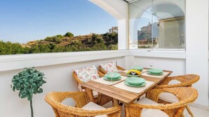 Un balcón con sillas de mimbre y una mesa lista para comer, con vistas a un paisaje montañoso.