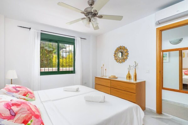 A bedroom with a bed, a dresser, a mirror, and a window with curtains.