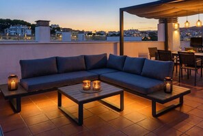 A rooftop terrace with a sofa, two tables, and hanging lights.