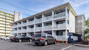 A multi-story hotel with balconies, a parking lot, and a neighboring building. - Beach view condo with private deck (Ocean City)