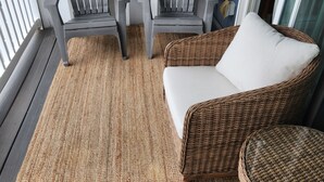 A balcony with two grey Adirondack chairs, a wicker sofa with white cushions, and a woven rug on a wooden deck. - Beach view condo with private deck (Ocean City)