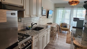 A modern kitchen with white cabinets, a stainless steel refrigerator, a granite countertop, and a dining area with a wooden table and chairs. - Beach view condo with private deck (Ocean City)