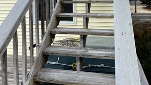 Eine Holztreppe führt zu einem Gebäude mit weißer Brüstung und gelber Fassade.