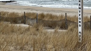 Ein Strand mit einer Holzlattenzaun und einem Schild mit der Aufschrift 'KENTFORD AVE'.