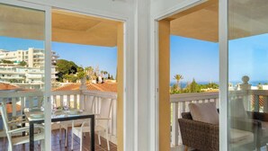 A balcony with a table and chairs, a wicker sofa, and a view of the sea and buildings. - Lovely seaview apartment by Costarentals - Ref 106 (Benalmádena)
