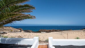Vista de una playa con costa rocosa, cielo despejado y una estructura blanca al frente.