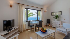 Un salón moderno con televisión, asientos, comedor y vista al mar.