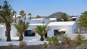 Un complejo turístico en la costa con edificios blancos, palmeras y una montaña al fondo.