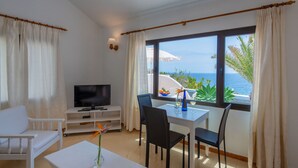 Una habitación con televisión, mesa de comedor, sillas y vistas al mar.