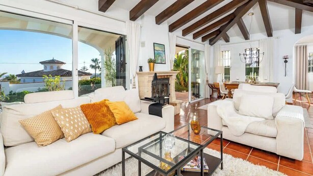 A spacious living room with a white sofa, a glass coffee table, and a fireplace. There is a dining area with a table and chairs visible in the background. - Urb Villa with pool by Costarentals- Ref 139 (Mijas)