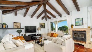 A living room with a fireplace, white sofas, a TV, and a large window. - Urb Villa with pool by Costarentals- Ref 139 (Mijas)
