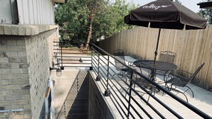 Een terras buiten met een metalen tafel en stoelen, een zwarte parasol en een houten hek op de achtergrond.