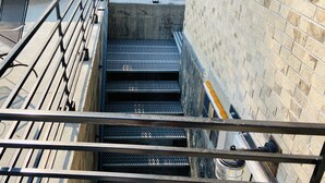 Een set metalen trappen met een gaasvloer, die naar een lager niveau leiden.