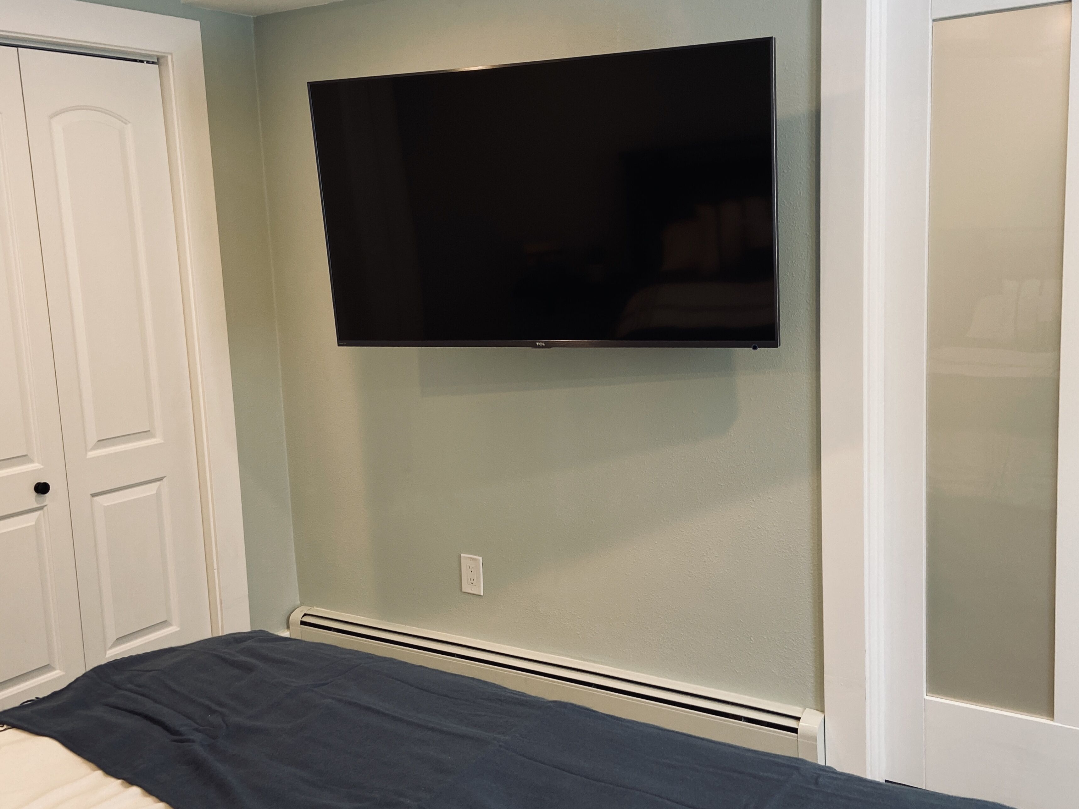 Ein Schlafzimmer mit einem Bett, einem an der Wand befestigten Fernseher und einer weißen Tür.