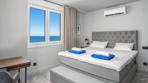 Een hotelkamer met een groot bed, een bureau, een stoel en uitzicht op zee.