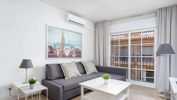 A modern living room with a grey sofa, white coffee table, and a cityscape painting. - Central Gem Los Boliches by Costarentals - Ref 77 (Costa del Sol)