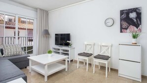 A modern living room with a sofa, a white coffee table, two white chairs, a TV, a clock, and a plant. - Central Gem Los Boliches by Costarentals - Ref 77 (Costa del Sol)