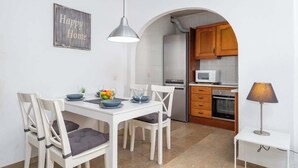 A dining area with a white table and chairs, a kitchen with wooden cabinets and appliances, and a 'Happy Home' sign on the wall. - Central Gem Los Boliches by Costarentals - Ref 77 (Costa del Sol)
