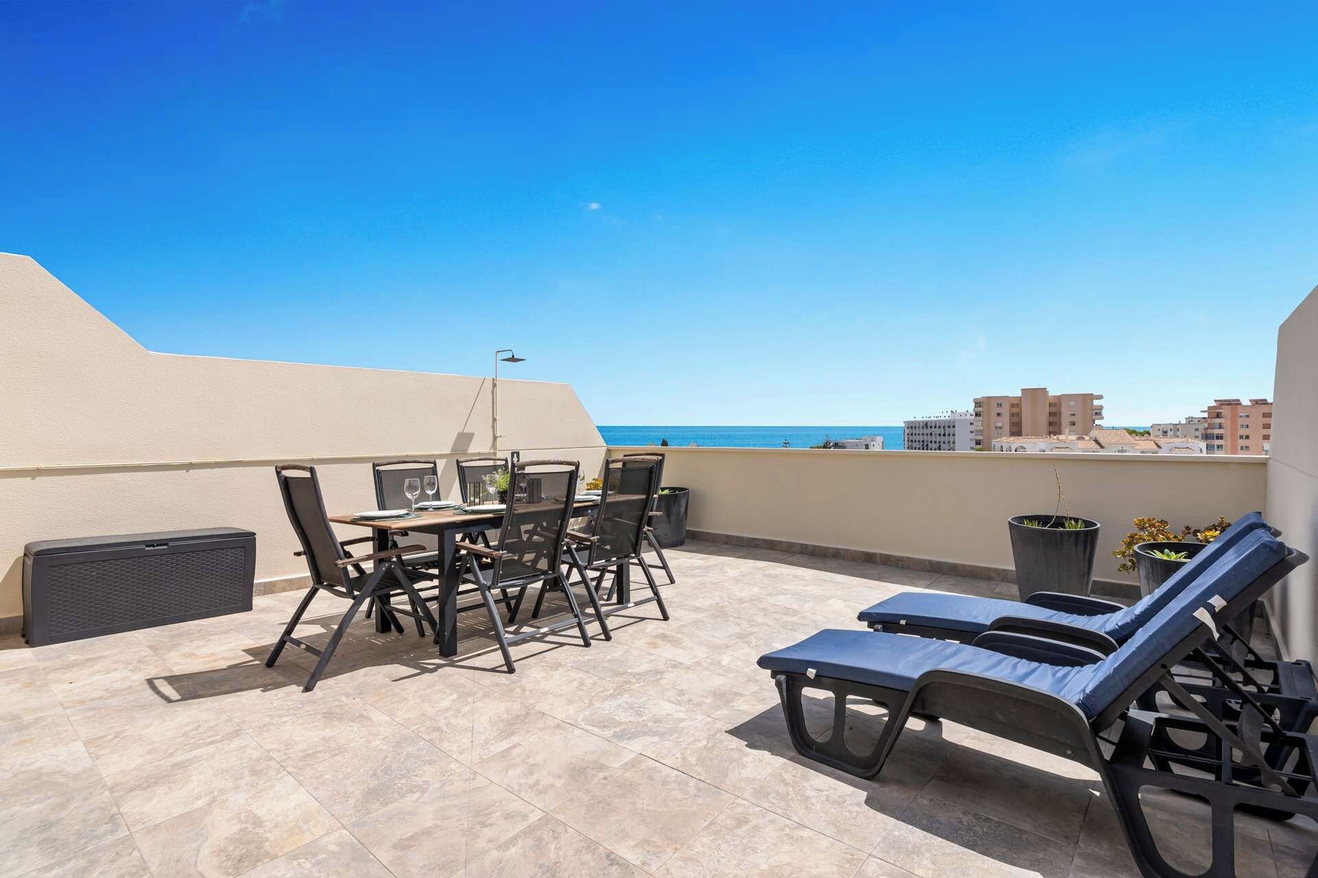 Una terraza en la azotea con mesa y sillas, sillones de descanso y vistas al mar.