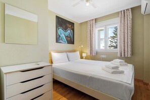 A hotel room with a bed, a bedside table, a lamp, a painting, and a window with curtains.