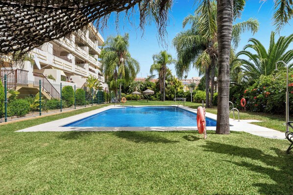 A swimming pool surrounded by well-maintained grass, palm trees, and a multi-story building with balconies.