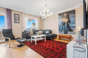 Un salon avec un canapé en cuir noir, une table basse blanche, un tapis à motifs rouges, un fauteuil en cuir noir et un grand tableau accroché au mur.