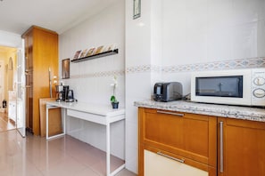 A modern kitchen with white tiles, a microwave, a toaster, and a coffee maker.