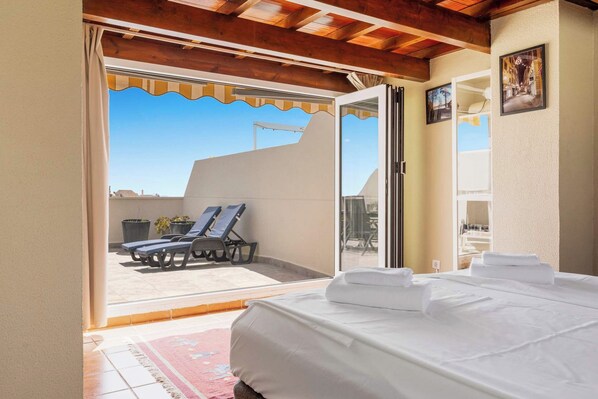 Une chambre d’hôtel avec un lit, une vue sur le balcon extérieur avec des fauteuils de jardin, et une porte donnant sur le balcon.