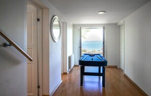 Un pasillo con mesa de billar, una puerta con espejo y una ventana con vista al mar.